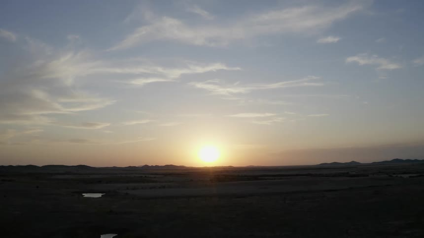 A landscape with puddles of water with the sun the sky and clouds in the background
