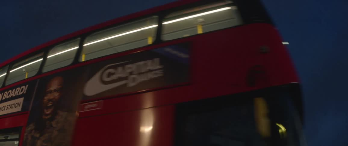 A pair of double decker buses travel through an intersection in a city at night
