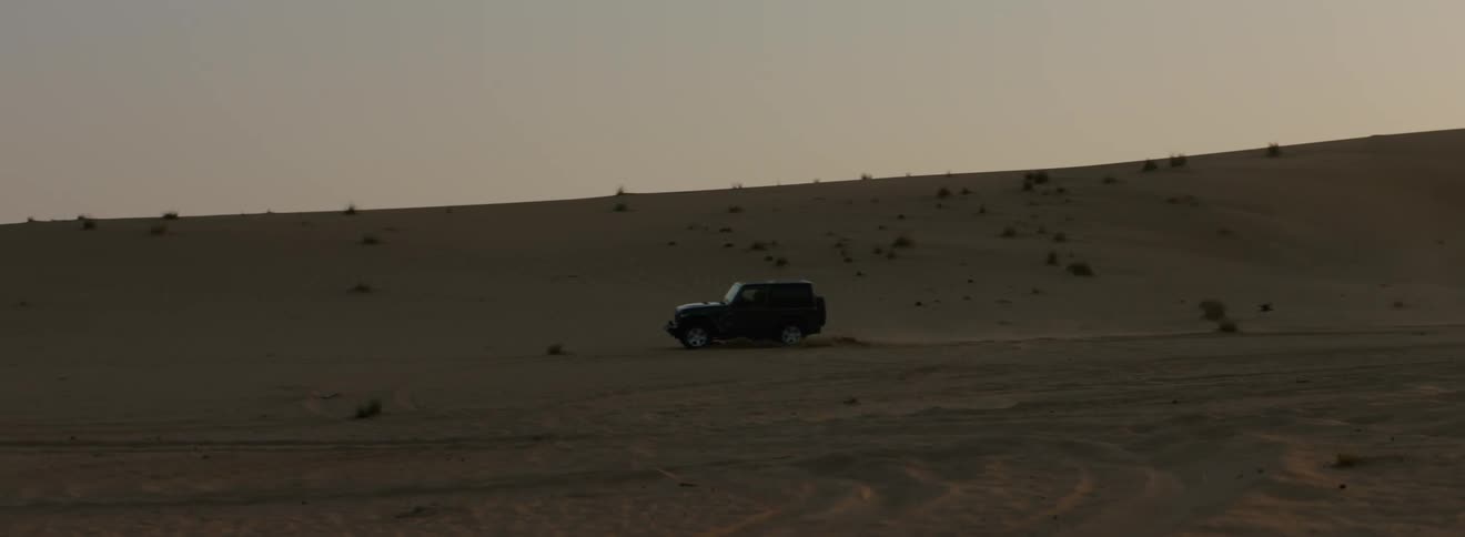 A jeep is driving around in the sand near some dunes