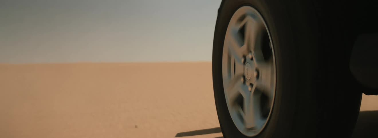 An automobile tire is spinning as it travels across sand