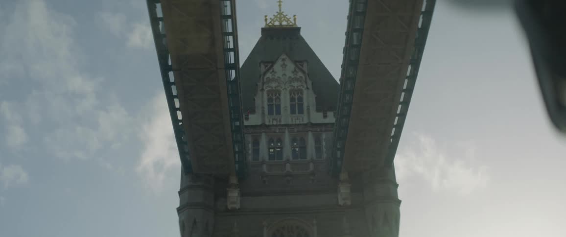 Traffic flows through town over bridge through arch topped by building on bright day