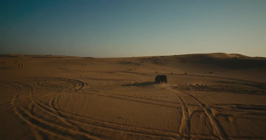 An aerial view of a sports utility vehicle traveling on a desert landscape during the daytime