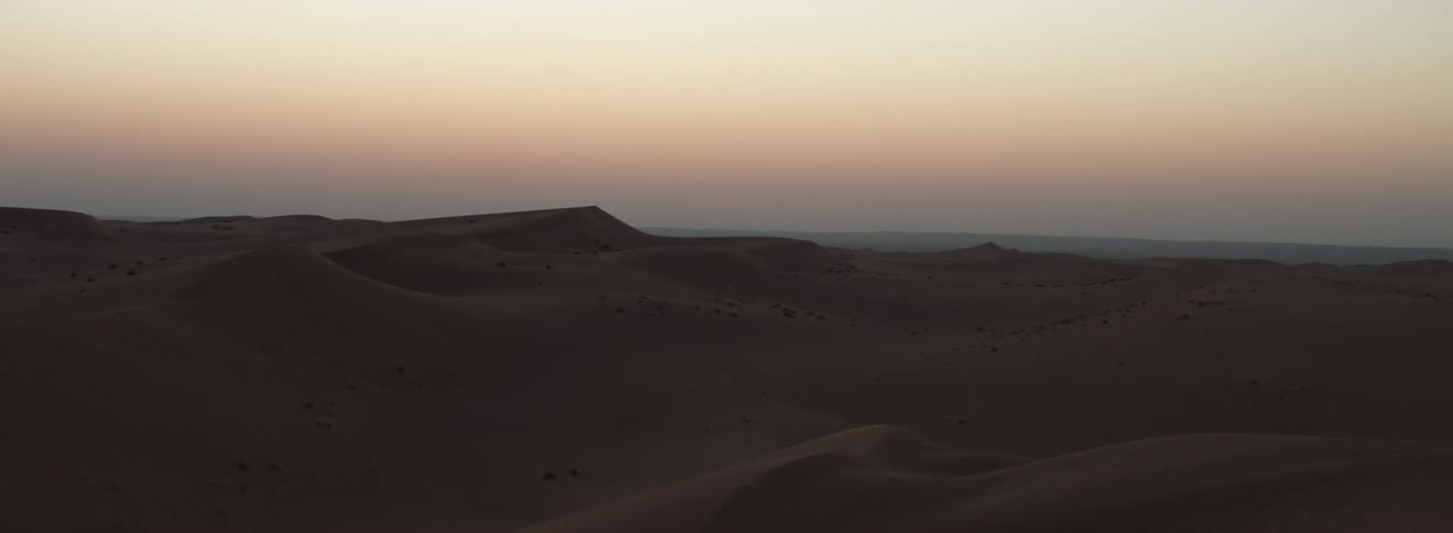 A landscape view of a sandy desert at sunset
