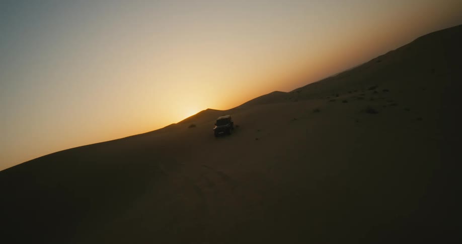 A jeep drives through sand dunes in the desert
