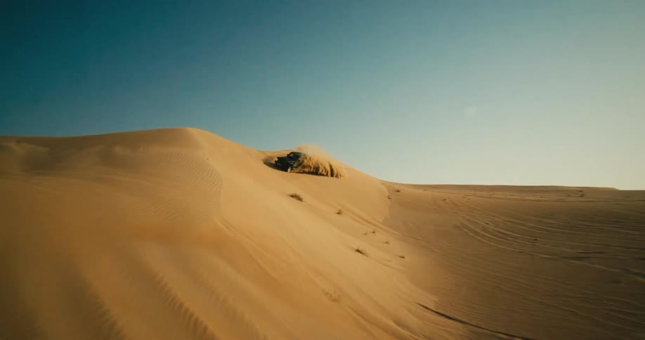 A vehicle kicks up a cloud of sand behind it as it travels off road across dunes in the desert during the day