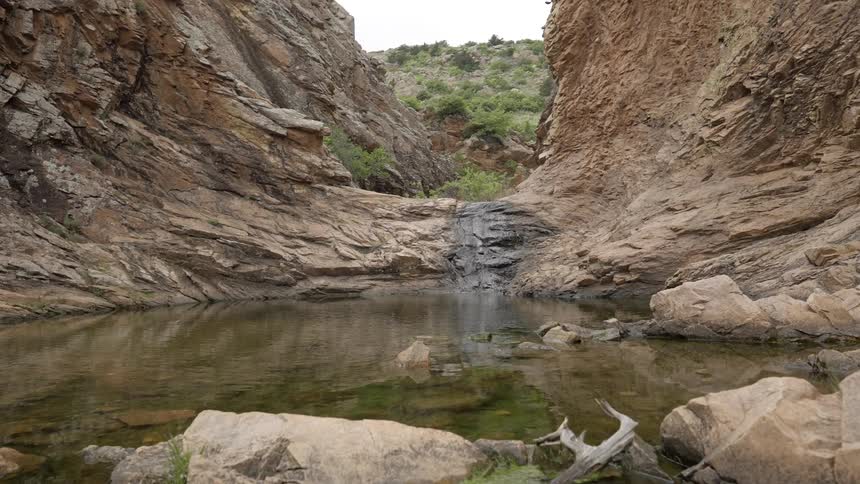 A stream is flowing into a small pond in a rocky canyon during the day
