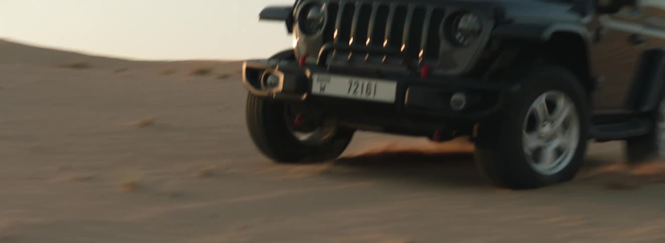 A car driving over sand in a remote desert at sunset