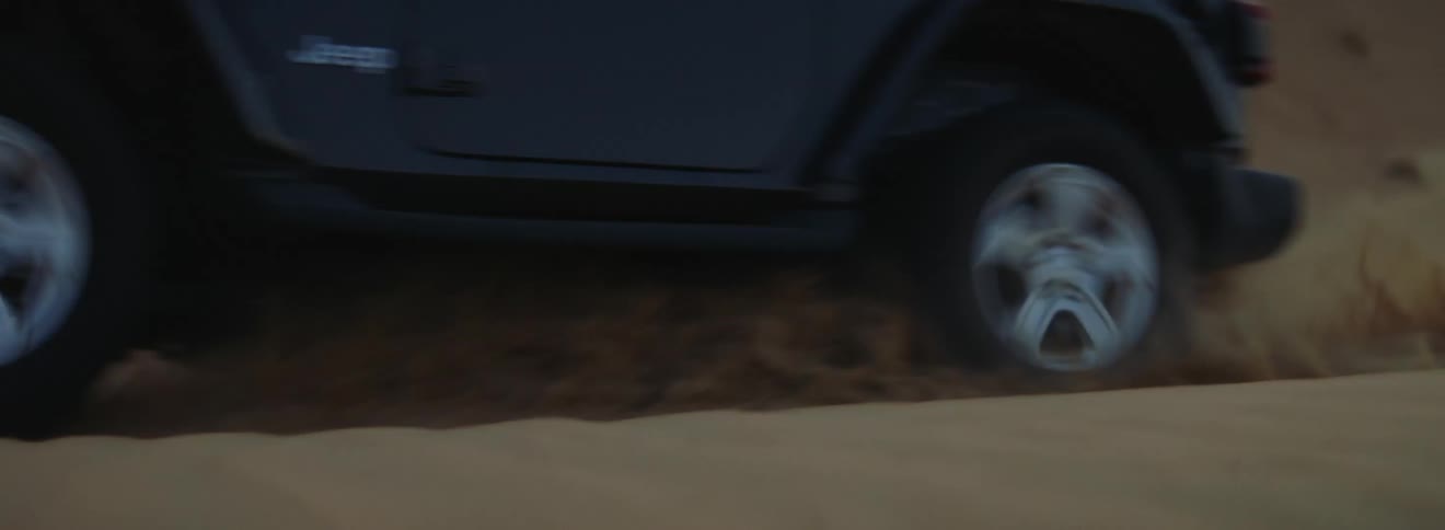 Black jeep rides across desert slope spewing sand