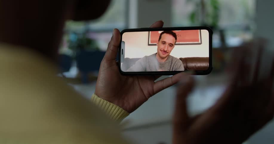 Woman with short hair and yellow sweater holds smartphone and makes a video call in living room
