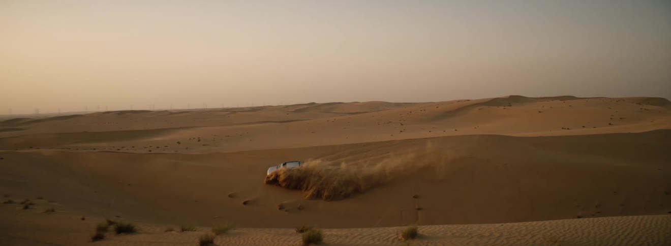 A car driving over sand dunes in a remote desert at dawn