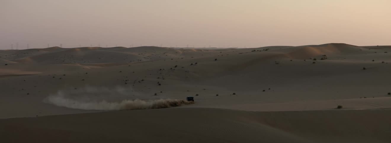 A vehicle driving in a desert with dunes with the sky and clouds in the background