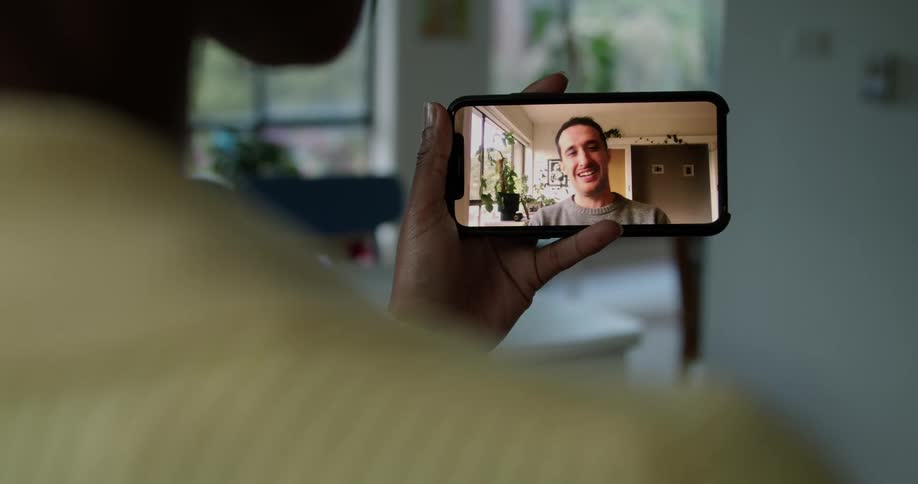 A person in a room on a smart phone with a wall a doorway and a plant in the background