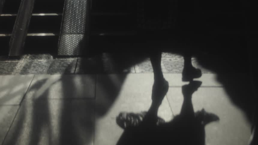 People are walking inside a building near a stairway during the day and casting shadows onto the floor