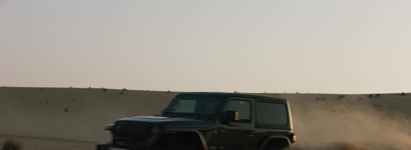 A jeep does donuts in the desert and kicks up a wall of sand