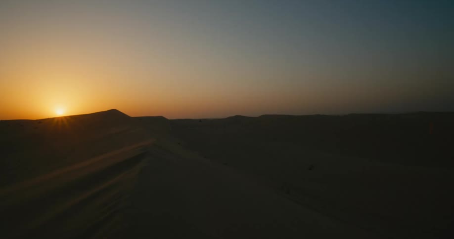 Sand dunes and desert are silhouetted against the sunset