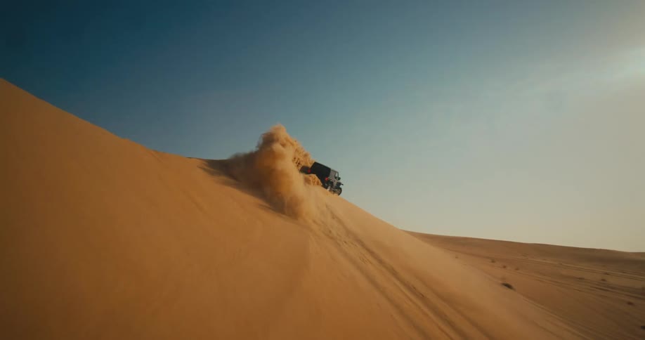 Black jeep rides up and down desert dune spewing sand into air on sunny day