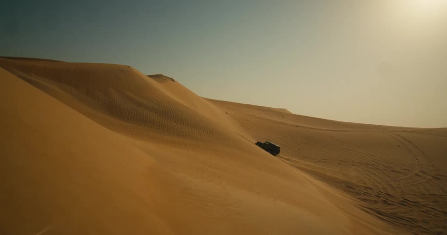 A jeep is driving up and down large sand dunes