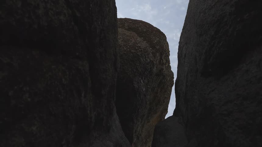 Sky with small puffy clouds shows through crevice in stone mountains with shadowy depressions