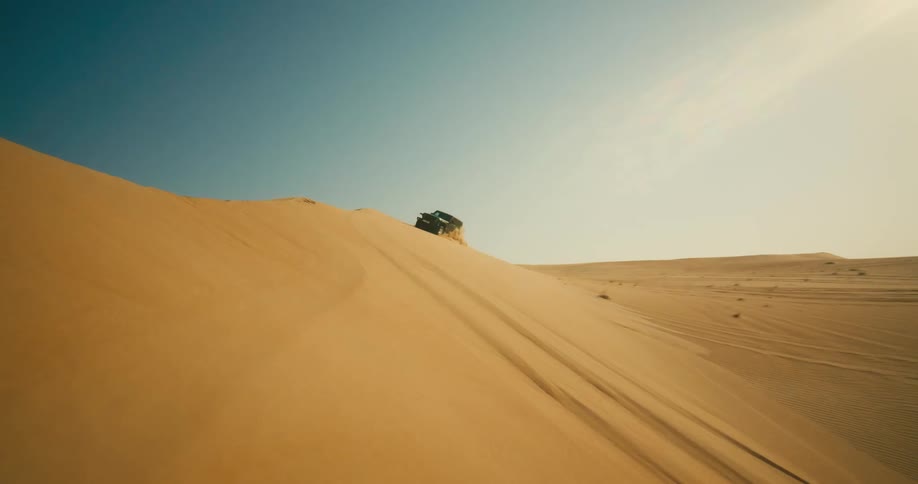 A jeep is driving up a hill in the dunes and is spraying sand