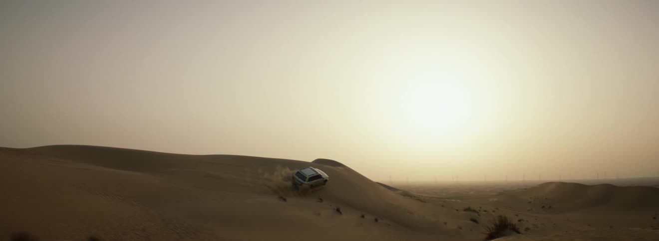 A vehicle rides on the side of the dune in the desert
