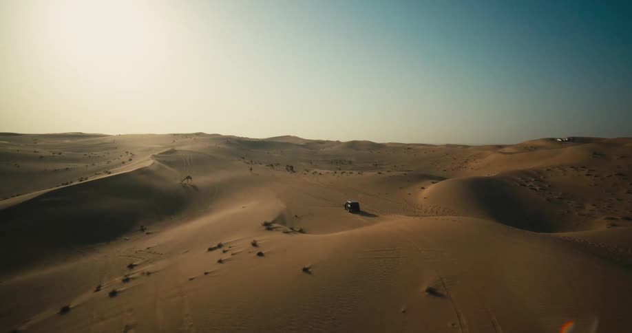 A jeep drives through sand dunes in the desert