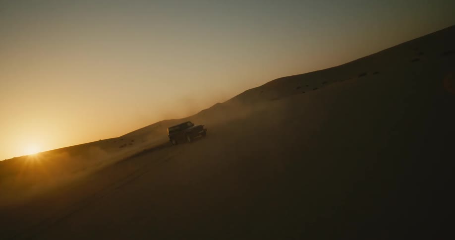 A vehicle driving across a desert as the sun sets