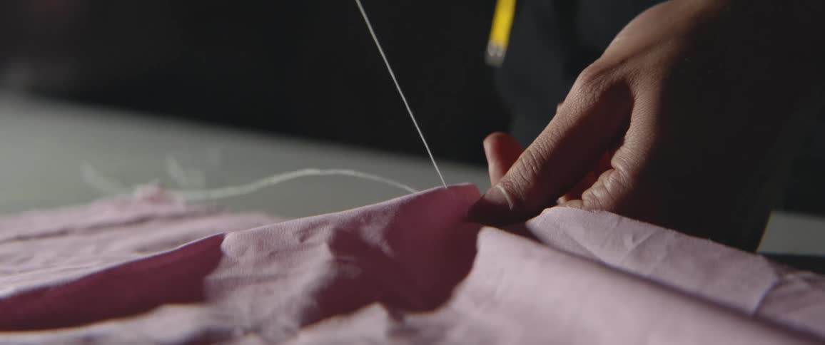 Someone is sewing pink fabric with white thread on a table