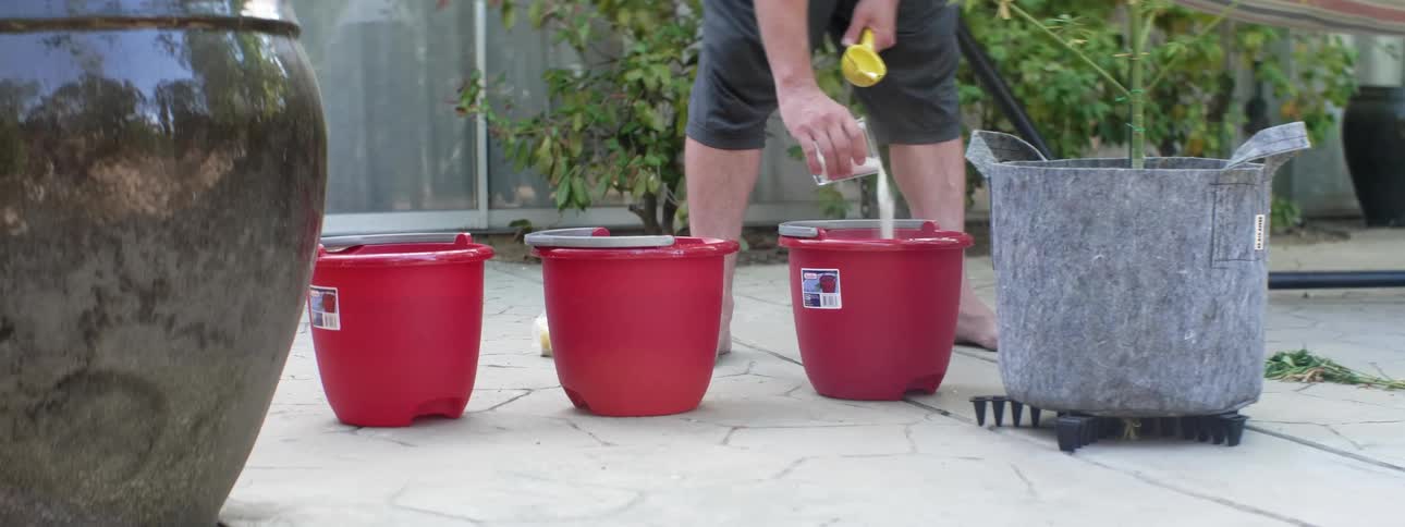 Someone is pouring white powder into red buckets sitting outside on the pavement