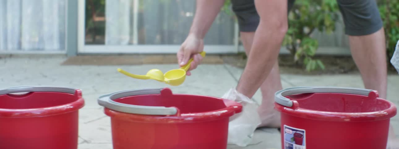 Man squeezes juice into red buckets using juicer while standing in backyard