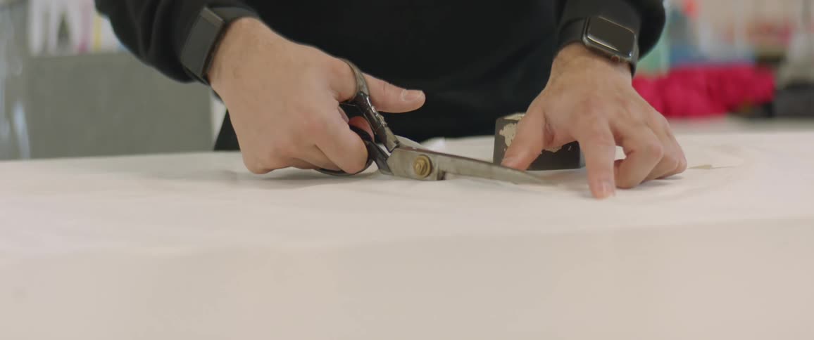 A person in a room using a scissors to cut a sheet of paper with a wall in the background