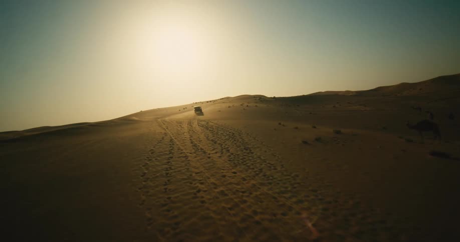 A black truck travels across a desert with the sun on the horizon