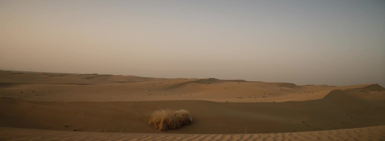 Gray car drives fast on the edge of sand dune in the desert
