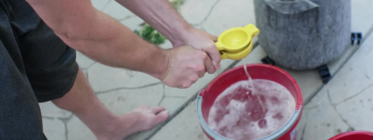 A man squeezing lemon juice into a bucket of water outside
