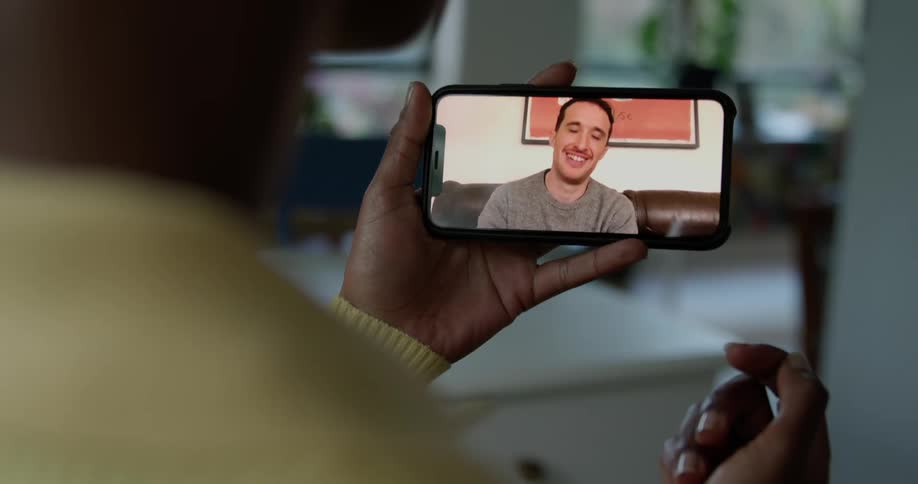 A person in a room on a smart phone with a wall a doorway and a plant in the background