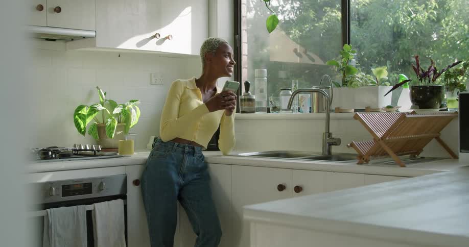 A young woman laughs while using her smartphone in the kitchen during the day