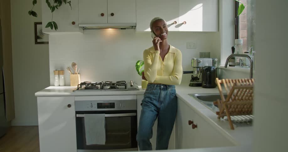 A woman leans against her kitchen counter while talking on the phone