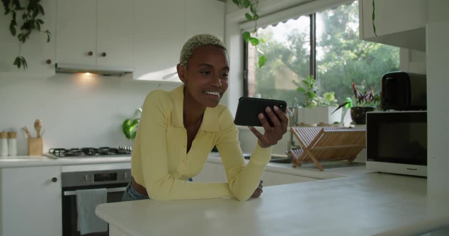A woman smiling while talking on a video call in a home kitchen