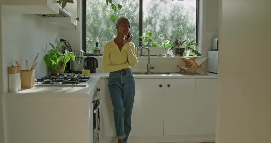 A woman is leaning against a kitchen counter while smiling and talking on cell phone
