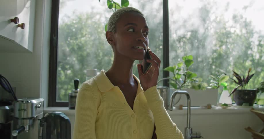 A woman stands in her kitchen and laughs as she talks on her cell phone
