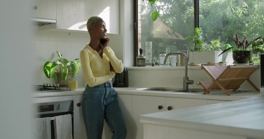 A woman answers her phone while shes standing in her kitchen