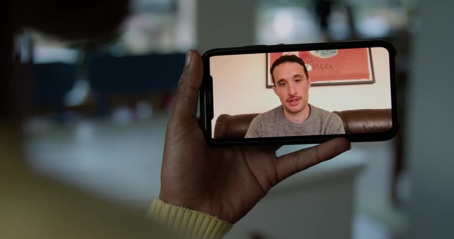 A person in a room on a smart phone with a wall a doorway and a plant in the background