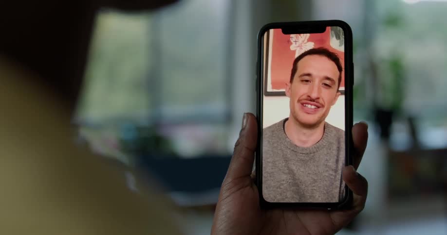 Woman with short hair and yellow vest makes video call on smartphone with man wearing gray sweater