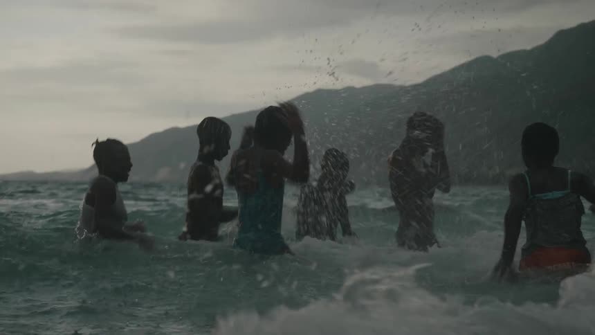 A group of children splashing each other in the ocean at dusk