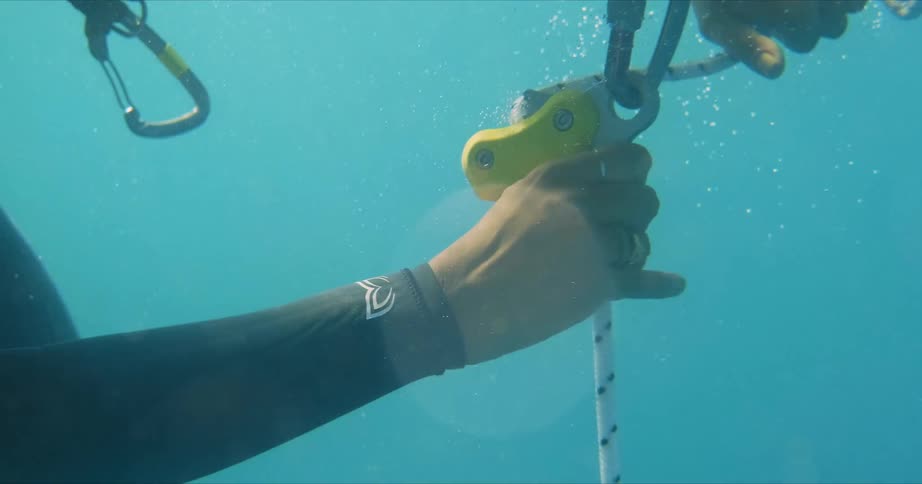 A scuba diver is underwater tying a rope to a latch