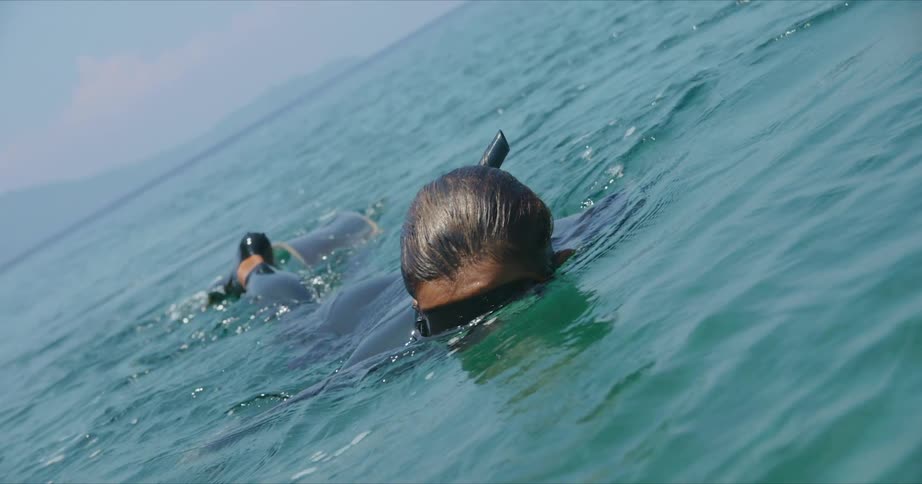 A swimmer is snorkeling with their face in the water and diving fins on their feet