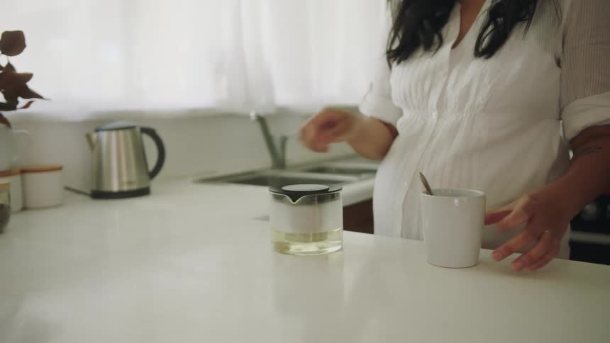 A woman in a kitchen putting a spoon inside a mug on a counter