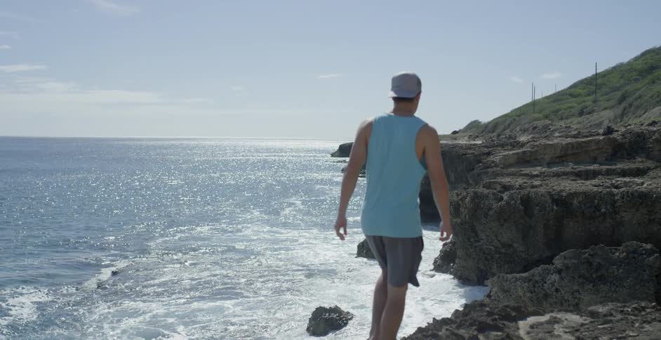 A man in a blue shirt walks down a rocky shore