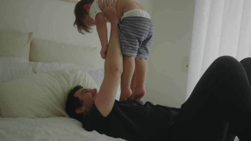 A man playing with a boy on a bed with a wall and window in the background