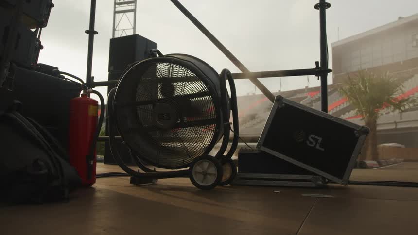 A fan on a stage blowing smoke with the sky and clouds in the background