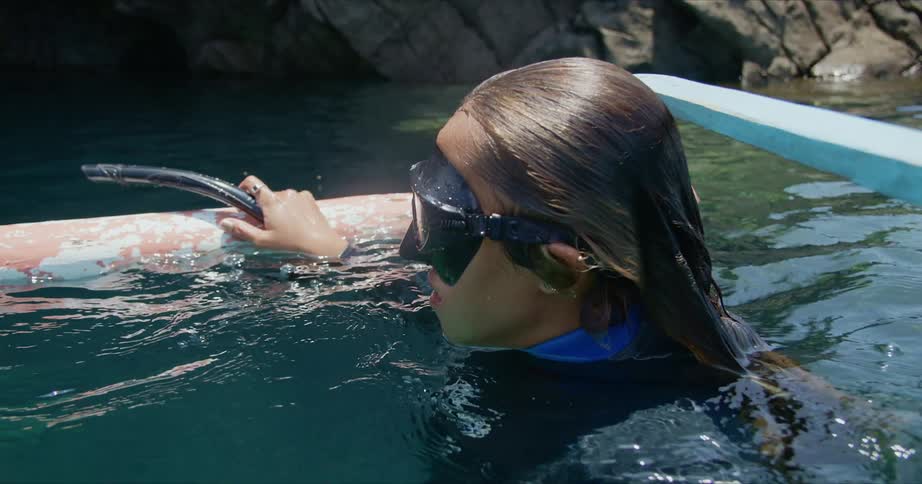 A snorkeler takes a break and rests while holding onto a pipe in the ocean
